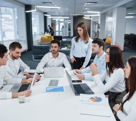 Guy on the left side talking and colleagues is listening to him. Group of young freelancers in the office have conversation and smiling.